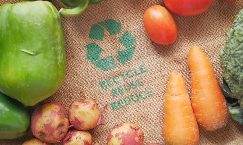 Fresh vegetables on a burlap bag with recycle symbol, promoting eco-friendly choices.